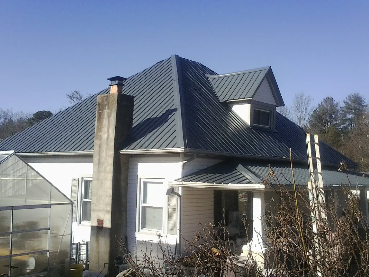 Dark blue standing seam metal roof on a white farmhouse with dormer — Slate & Tile Roof Repair by Roofing Brothers in Mound