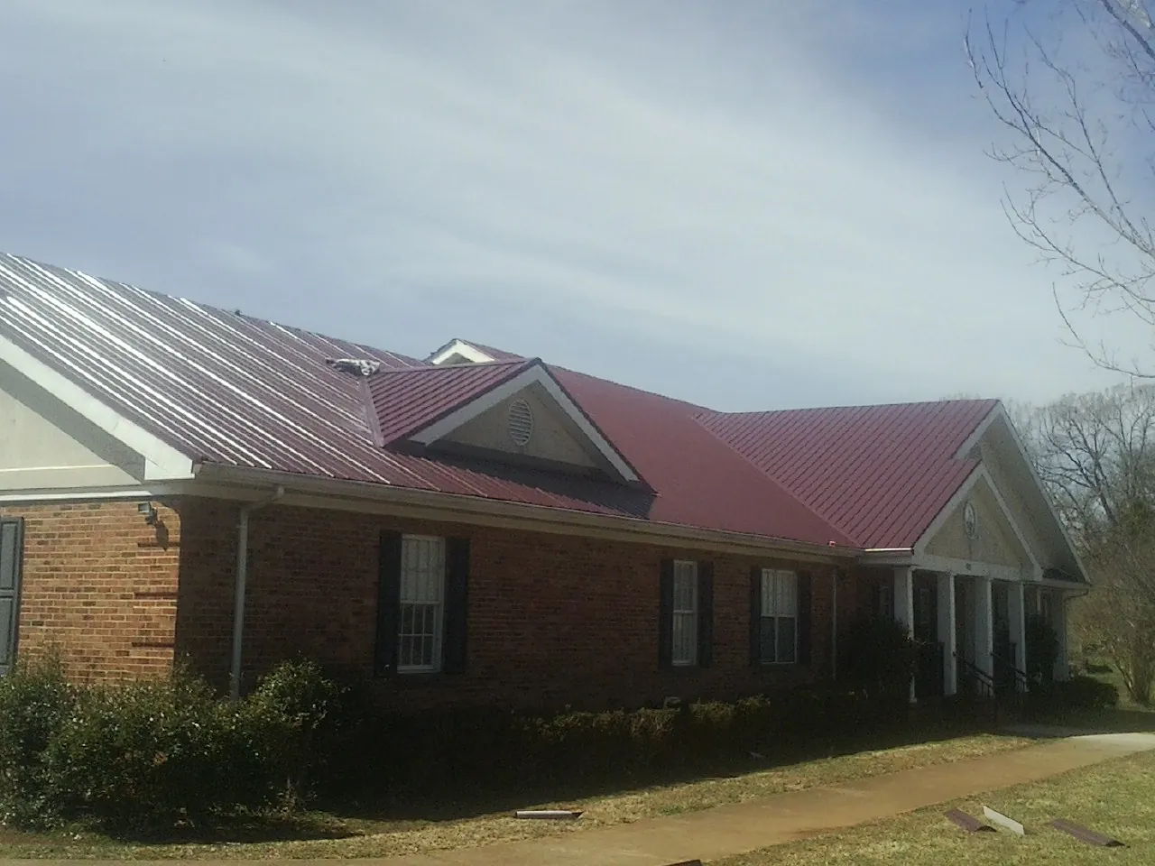 Red metal roof with gabled entries on a long brick building, from a Hail Damage Roof Repair job in Mound