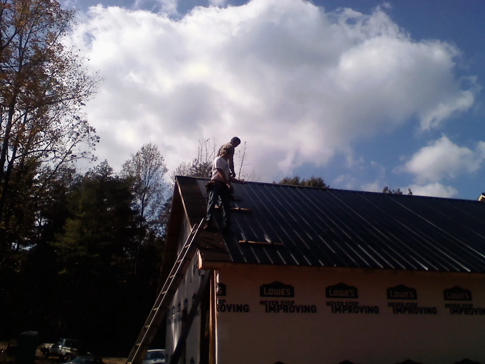 Roofer fastening dark metal panels high against a cloudy sky, from a Roof Inspection job in Mound
