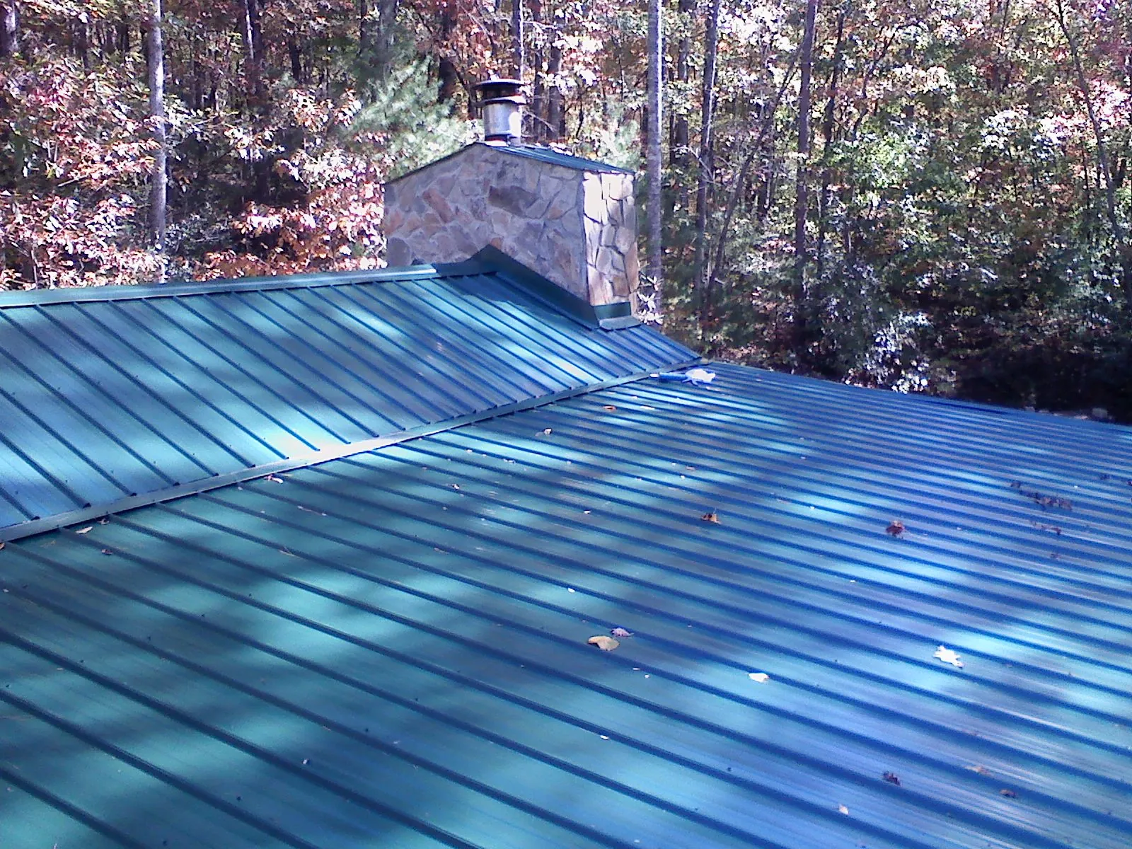 New green metal roof and stone chimney surrounded by autumn woods in Mound